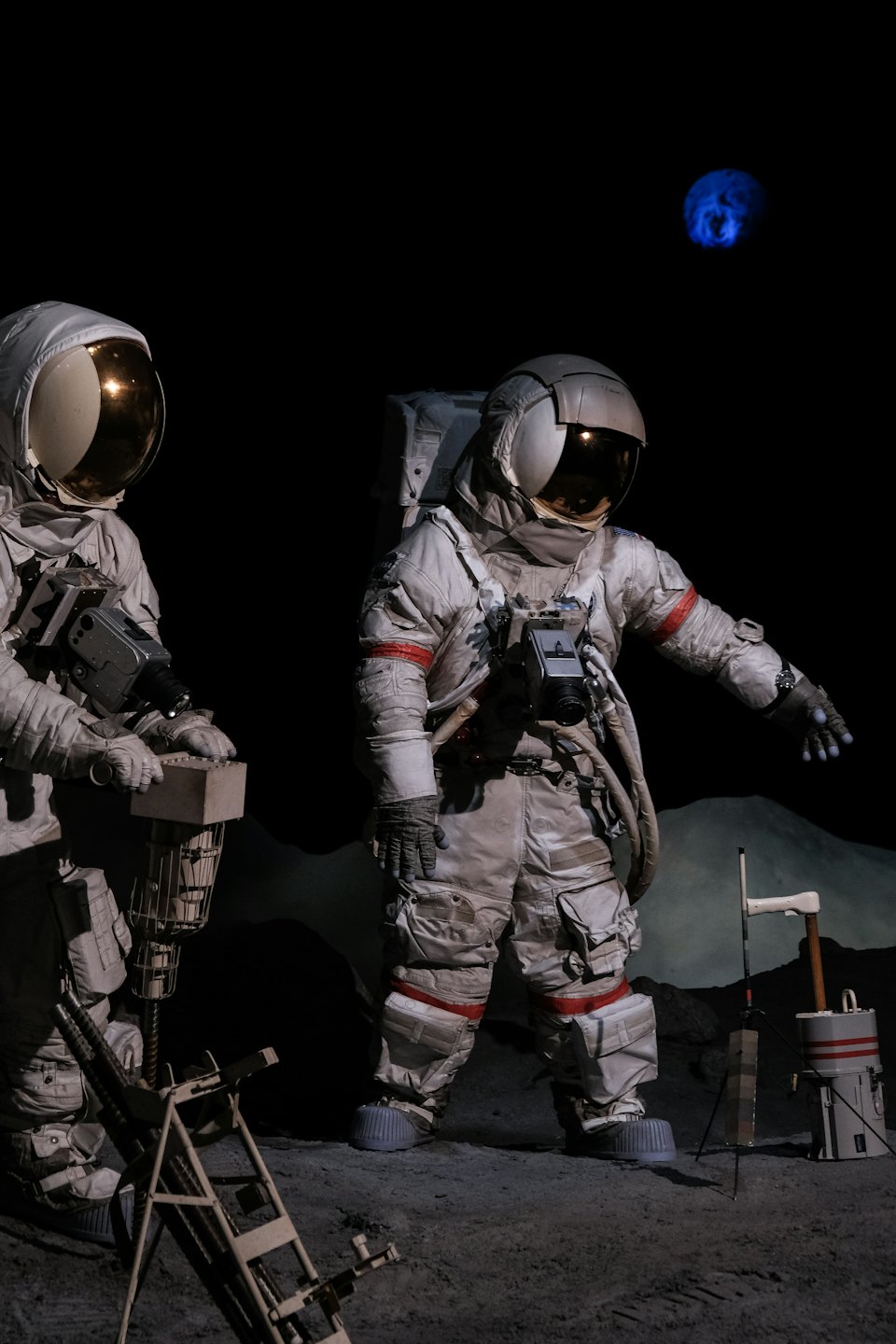 Astronauts in museum exhibit with lunar landscape and planet.